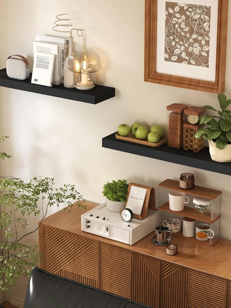 Minimalist black floating shelves mounted securely above a cabinet in a modern living room, serving as the best shelves for an organized display of books, lamps, and seasonal gallery items.